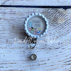 May include: White badge reel with a white bottle cap featuring a pharmacy themed design with the text "Pharmacy Squad".