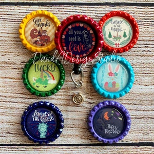 May include: Set of ten colourful bottle cap badges with various designs and sayings. The designs include a unicorn, a bunny, a pumpkin, a heart, a tree, a star, and a cat. The sayings include "Give thanks", "All you need is love", "Believe in the magic", "Lucky", "Hoppy Easter", "Land of the free", and "Happy Halloween".