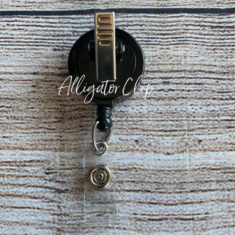 May include: Black retractable badge holder with a silver alligator clip and a clear plastic badge holder. The text "Alligator Clip" is printed on the badge holder.