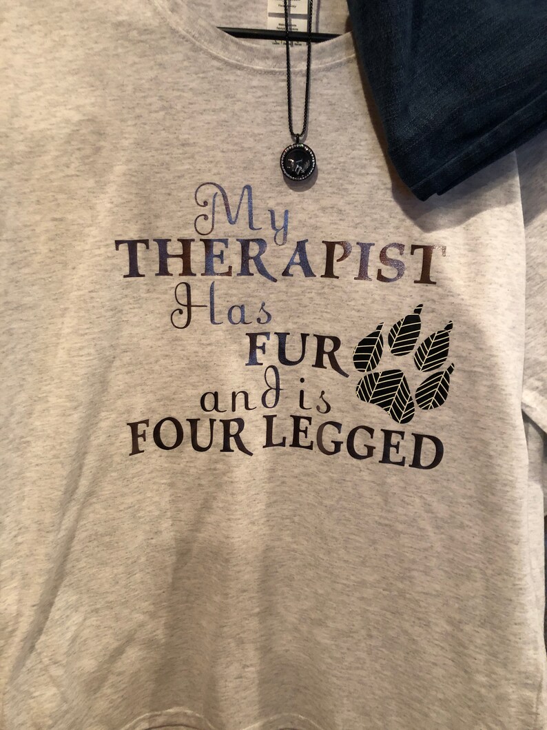 Puede incluir: Sudadera gris con el texto "Mi terapeuta tiene pelo y es de cuatro patas" y un gr&aacute;fico de una huella de pata.