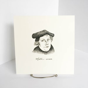 K&ouml;nnte beinhalten: Ein Schwarz-Wei&szlig;-Portr&auml;t von Martin Luther, der einen Hut und einen dunklen Mantel tr&auml;gt. Der Name "Martin LUTHER" ist unter dem Portr&auml;t in Kursivschrift auf einem cremefarbenen quadratischen Papier geschrieben.