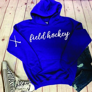 May include: A royal blue hooded sweatshirt with the text "field hockey" in white on the front. The left sleeve has a white graphic of two crossed hockey sticks.