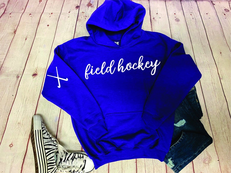 May include: A royal blue hooded sweatshirt with the text "field hockey" in white on the front. The left sleeve has a white graphic of two crossed hockey sticks.