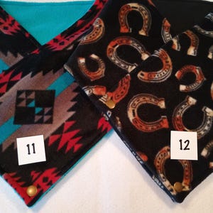 K&ouml;nnte beinhalten: Zwei Fleece-Halsw&auml;rmer mit unterschiedlichen Mustern. Einer ist schwarz mit einem roten, wei&szlig;en und braunen geometrischen Muster und der andere ist schwarz mit einem braunen Hufeisenmuster. Beide haben ein t&uuml;rkisfarbenes Fleecefutter und einen goldenen Druckknopf. Die Halsw&auml;rmer sind mit den Nummern 11 und 12 gekennzeichnet.
