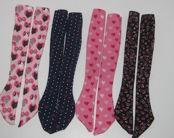 May include: Four pairs of knee-high socks with different patterns. One pair features a pink background with white hearts and black cats. Another pair has a navy blue background with white polka dots. The third pair has a pink background with white hearts. The final pair has a black background with white hearts and pink accents.