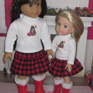 May include: Two dolls wearing red and black plaid skirts and white long-sleeved shirts with a cat graphic. The dolls are wearing red boots with white fur trim. The dolls are standing on a patterned rug.