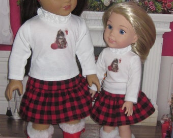 May include: Two dolls wearing red and black plaid skirts and white long-sleeved shirts with a cat graphic. The dolls are wearing red boots with white fur trim. The dolls are standing on a patterned rug.