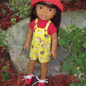May include: A doll wearing a red and white polka dot hat, a red shirt, and yellow overalls with a chicken print. The doll has brown hair and brown eyes.