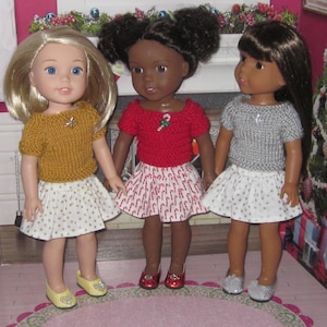 May include: Three dolls wearing holiday-themed outfits. The doll on the left is wearing a yellow sweater and a white skirt with gold polka dots. The doll in the middle is wearing a red sweater with a candy cane design and a white skirt with red candy canes. The doll on the right is wearing a silver sweater and a white skirt with silver polka dots.