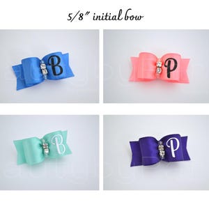 May include: Four 5/8 inch initial bows in different colors.  A blue bow with a white "B", a pink bow with a white "P", a light blue bow with a white "B", and a purple bow with a white "P". Each bow has a rhinestone in the center.