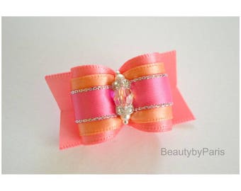Könnte beinhalten: Eine rosa und orangefarbene Schleife aus Satin mit silbernem Besatz und einem klaren Kristall-Verzierstück in der Mitte.