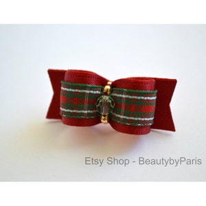 May include: A red, green, and white plaid ribbon bow with a clear crystal accent. The bow is attached to a red felt backing.
