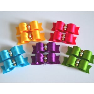 May include: Set of ten colorful satin ribbon bows with pearl accents. The bows are in shades of yellow, red, purple, blue, and green.