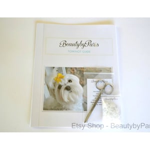 May include: A guide for creating a topknot on a dog, with a photo of a white dog with a yellow bow, a pair of scissors, and a small bag of white rubber bands. The guide is titled "Beautyby Par's Topknot Guide".