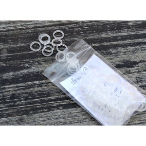 May include: A clear plastic bag filled with clear rubber bands. The bag is lying on a wooden surface. The text "Beau & P" is visible on the bag.