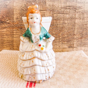 Vintage Made in Occupied Japan Porcelain Figurine Fancy Victorian Woman with Urn Planter. She wears ruffled skirts, ruffled sleeves, bow