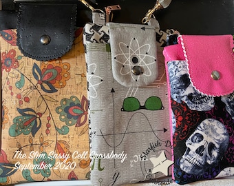 May include: Three different cell phone crossbody bags. The first bag is made of cork fabric with a floral pattern in shades of orange, red, blue, and green. The second bag is made of gray fabric with a science theme, including an atom, a graph, and the words "Starfish Design". The third bag is made of pink fabric with a skull and floral pattern in shades of black, white, red, and purple.