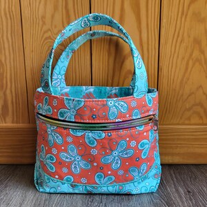 May include: A small turquoise and orange fabric tote bag with a zipper closure. The bag has a floral pattern and is perfect for carrying small items.