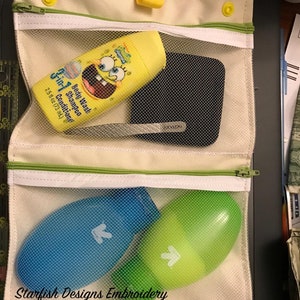 Könnte beinhalten: Eine weiße Reißverschlusstasche mit einem Netz-Innenfutter. Die Tasche hat zwei Fächer. Das obere Fach enthält eine gelbe Flasche mit Duschgel und Shampoo-Conditioner sowie ein schwarzes rechteckiges Objekt. Das untere Fach enthält eine blaue und eine grüne Flasche. Die Tasche hat gelbe Knöpfe an den Seiten und der Text "Starfish Designs Embroidery 8" x 12" Hoop" ist auf der Unterseite aufgedruckt.