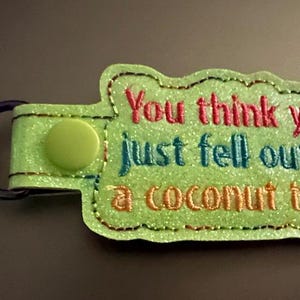 May include: A green keychain with a white stitched border and the text "You think you just fell out of a coconut tree?" in colorful embroidery.