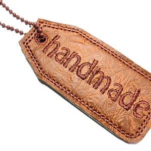 May include: A brown leather tag with a stitched border and the word "handmade" embroidered in brown thread.