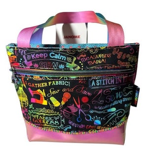 Könnte beinhalten: Eine schwarze Stofftasche mit einem regenbogenfarbenen Design mit Nähmotiven, Text und Illustrationen. Die Tasche hat eine Reißverschlusstasche und einen pinkfarbenen, schimmernden Boden.