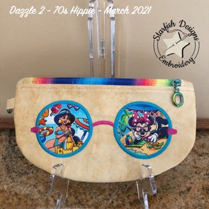 May include: A beige zippered pouch with a rainbow trim. The pouch features two round embroidered patches with a pink, blue, and white design. The left patch features a woman in a blue bikini and a crown. The right patch features a mouse with red polka dots and a bow. The text "Starfish Designs Embroidery" is embroidered on the pouch.