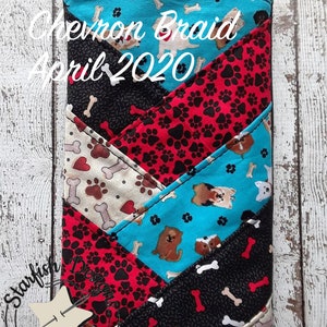 Op de afbeelding: Een zwarte en turquoise chevron-gepatroneerde stoffen tas met een ritssluiting en een zwarte band. De stof heeft een herhalend patroon van poot afdrukken, botten en honden. De tas heeft de tekst "Chevron Braid April 2020" op de voorkant.