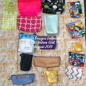 Può includere: Una collezione di pochette con cerniera colorate con vari disegni e motivi, tra cui cerchi, stelle e supereroi. Le pochette sono disposte su uno sfondo di tessuto con un motivo a stelle. Il testo "Starfish Designs Embroidery Flat Bottom Girl August 2019" è visibile al centro dell'immagine. Il testo "There's a size for it!" è visibile nella parte inferiore dell'immagine.