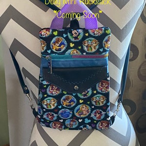 May include: A small black and blue mini backpack with a purple strap and a Disney character print featuring Mickey Mouse, Belle, and other characters. The text "Starfish Designs Dolly Mini Rucksack *Coming Soon*" is printed on the top of the backpack.