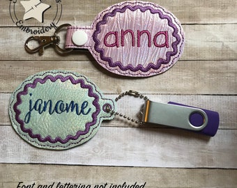 May include: Two oval-shaped keychains with scalloped edges. The top keychain is pink with the name "anna" embroidered in white. The bottom keychain is light blue with the name "janome" embroidered in dark blue. Both keychains have a silver metal ring.
