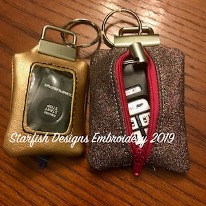 May include: Two keychains, one gold with a clear window and the text "ENGINE START STOP COMPLUSTAR", the other a sparkly gray with a pink zipper and a car key inside.