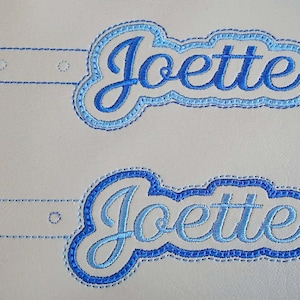 以下が含まれることがあります： 筆記体で「Joette」と刺繍された2つのパッチ。パッチは青色で、内側は水色、外側は濃い青色です。各パッチには、3つの小さな穴が開いたタブが付いています。