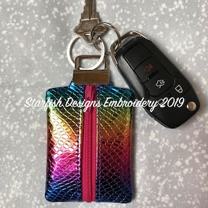 May include: A small rainbow iridescent zipper pouch with a pink zipper. The pouch is attached to a key ring with a house key and a car key.