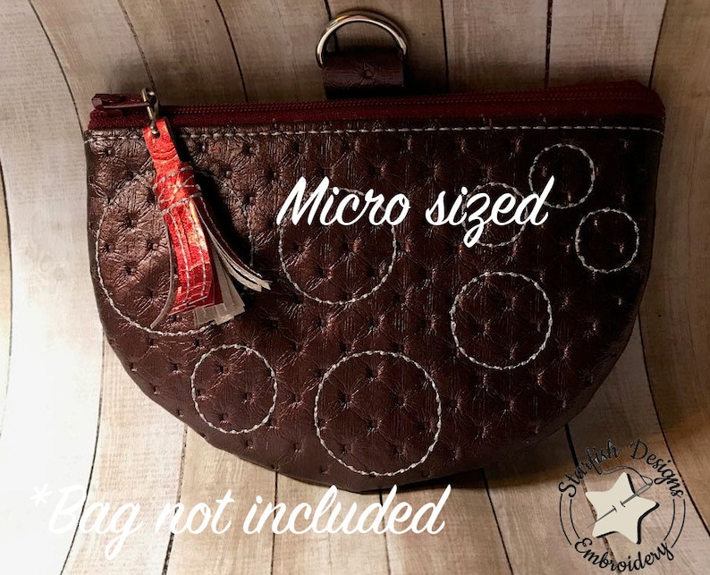 May include: A brown leather zippered pouch with a white tassel and white stitching in a circle pattern. The pouch is labeled "Micro sized".