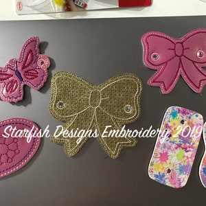 May include: Five embroidered patches with various designs, including a butterfly, two bows, a floral pattern, and two paint splattered patches. The patches are all pink, gold, and white with a white background.