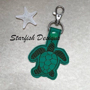 May include: Green leather keychain with a sea turtle design. The keychain has a silver metal clasp.
