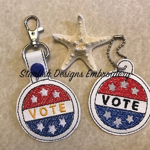 May include: Two round, white, red, and blue embroidered keychains with the word "VOTE" in yellow letters. Each keychain has three white stars on the top and bottom of the word "VOTE".