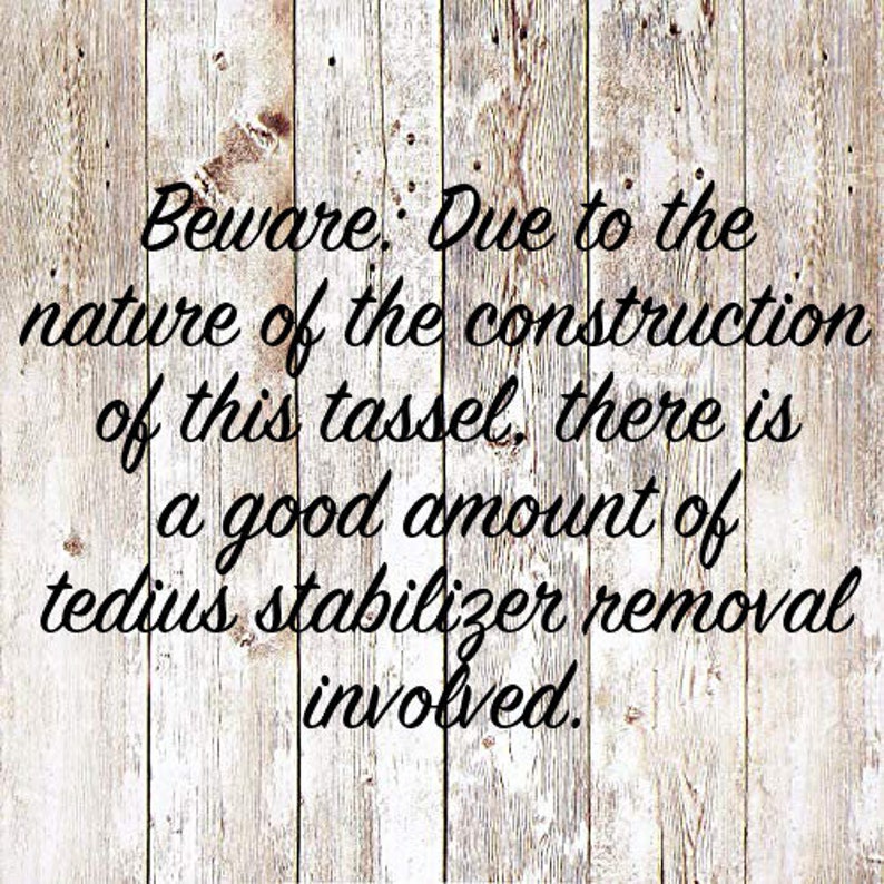 May include: A warning sign on a wooden background that reads: "Beware: Due to the nature of the construction of this tassel, there is a good amount of tedious stabilizer removal involved."