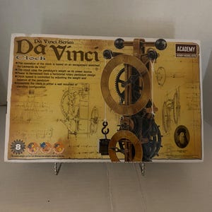 May include: A Da Vinci clock model kit box. The box features a detailed illustration of the clock's internal mechanisms, with gears and pendulum visible. Text on the box includes "Da Vinci Series" and "Academy Hobby Model Kits."