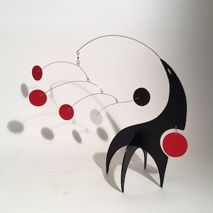 May include: A black and white yin yang mobile with red and white circles hanging from it. The mobile is suspended from a black stand with three legs.