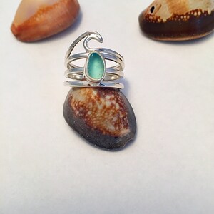 May include: Silver ring with a wave design and a teal blue sea glass stone.