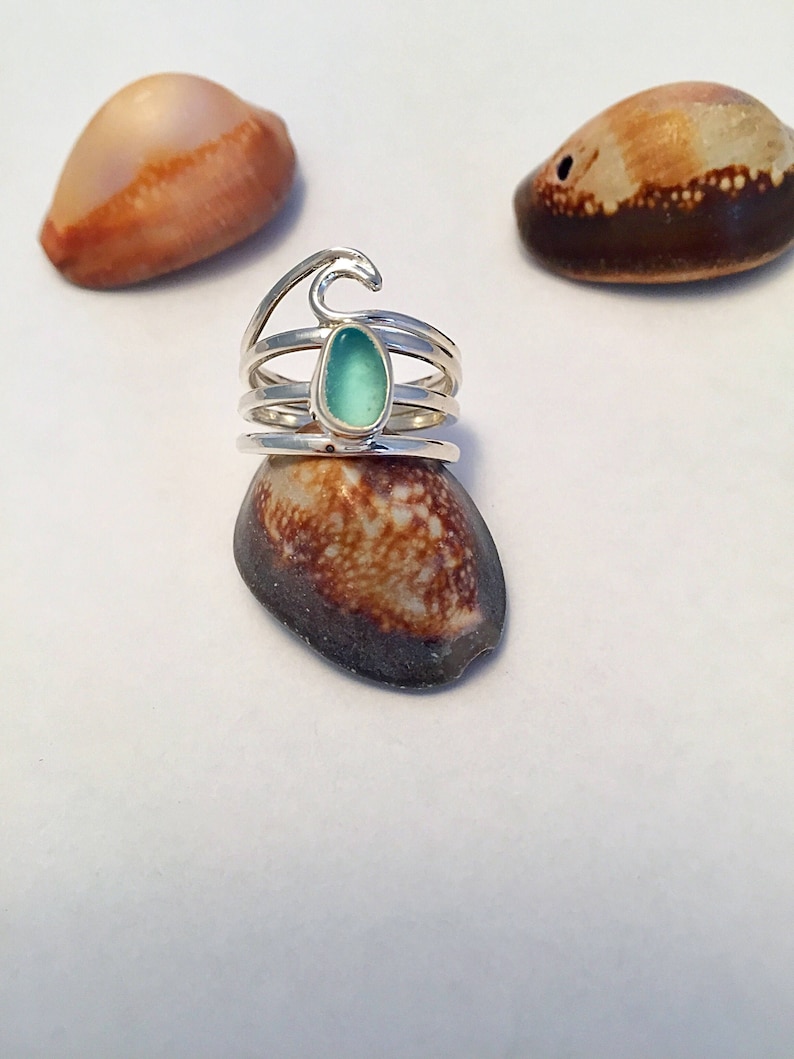 May include: Silver ring with a wave design and a teal blue sea glass stone.