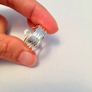 May include: A silver ring with a spiral design. The ring is made of multiple thin bands of metal that are twisted together to create a spiral shape.
