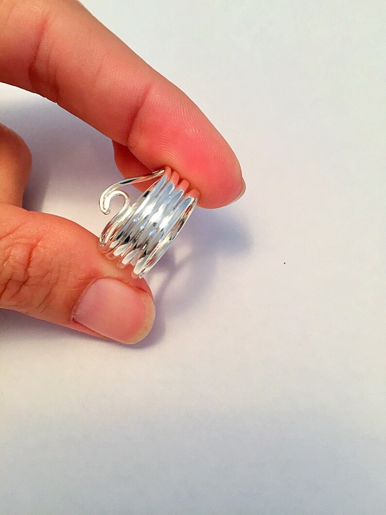 May include: A silver ring with a spiral design. The ring is made of multiple thin bands of metal that are twisted together to create a spiral shape.