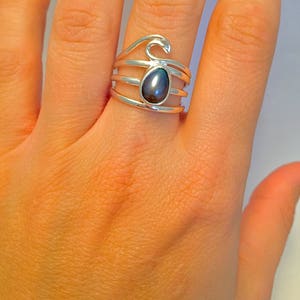 May include: A silver ring with a dark gray gemstone set in a wave design.