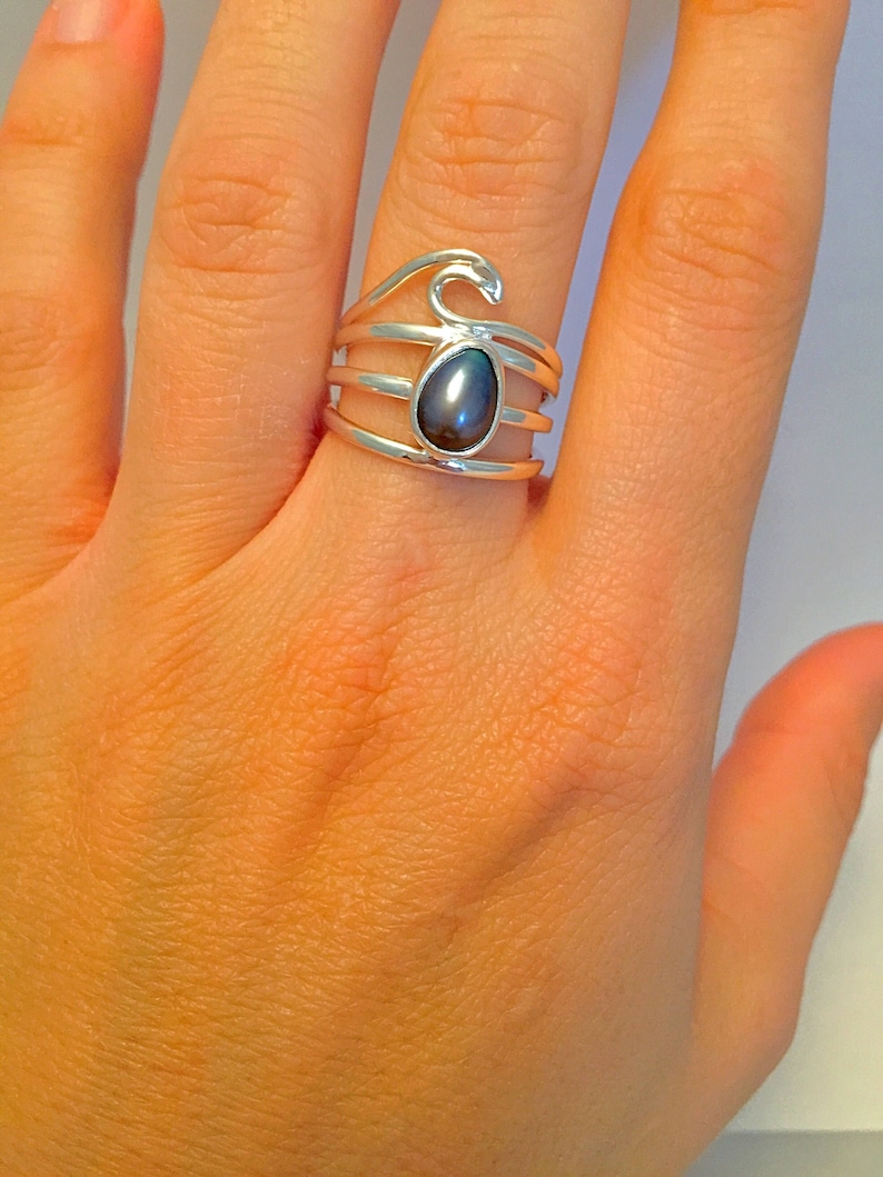 May include: A silver ring with a dark gray gemstone set in a wave design.