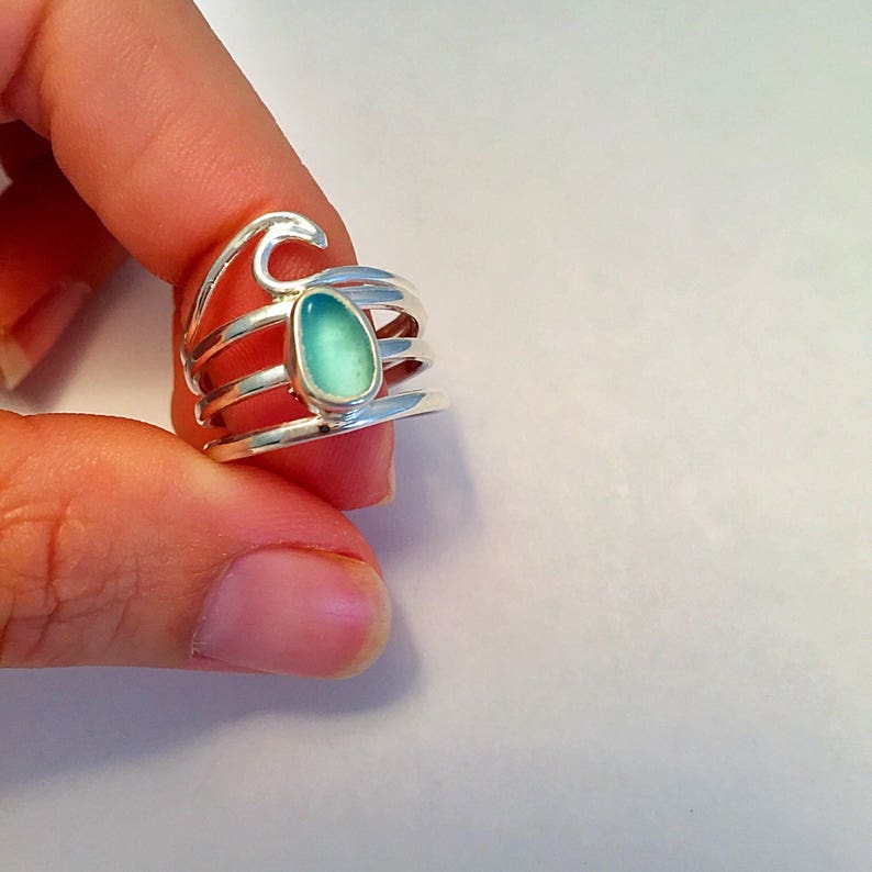 May include: A silver ring with a turquoise blue stone set in the center. The ring has a wave design on the top and three bands.
