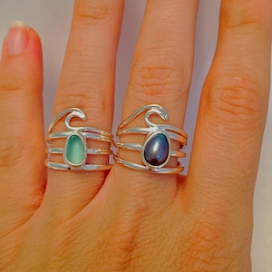 May include: Two silver rings with wave designs. One ring features a green gemstone, while the other has a black pearl.