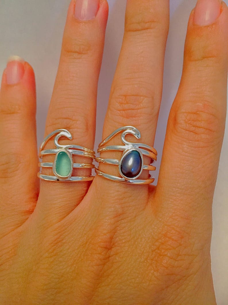 May include: Two silver rings with wave designs. One ring features a green gemstone, while the other has a black pearl.